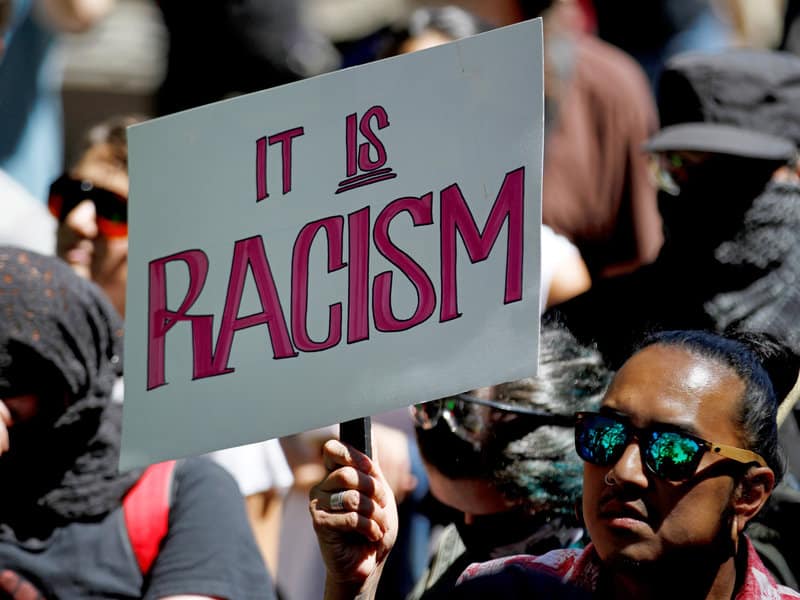 protestor holding a sign that says it is racism